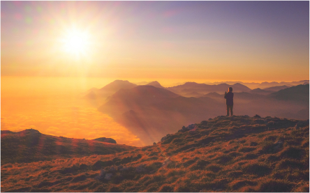 overlooking sunset on a ocean with a man on top of a mountain taking picture of the beatiful scenery